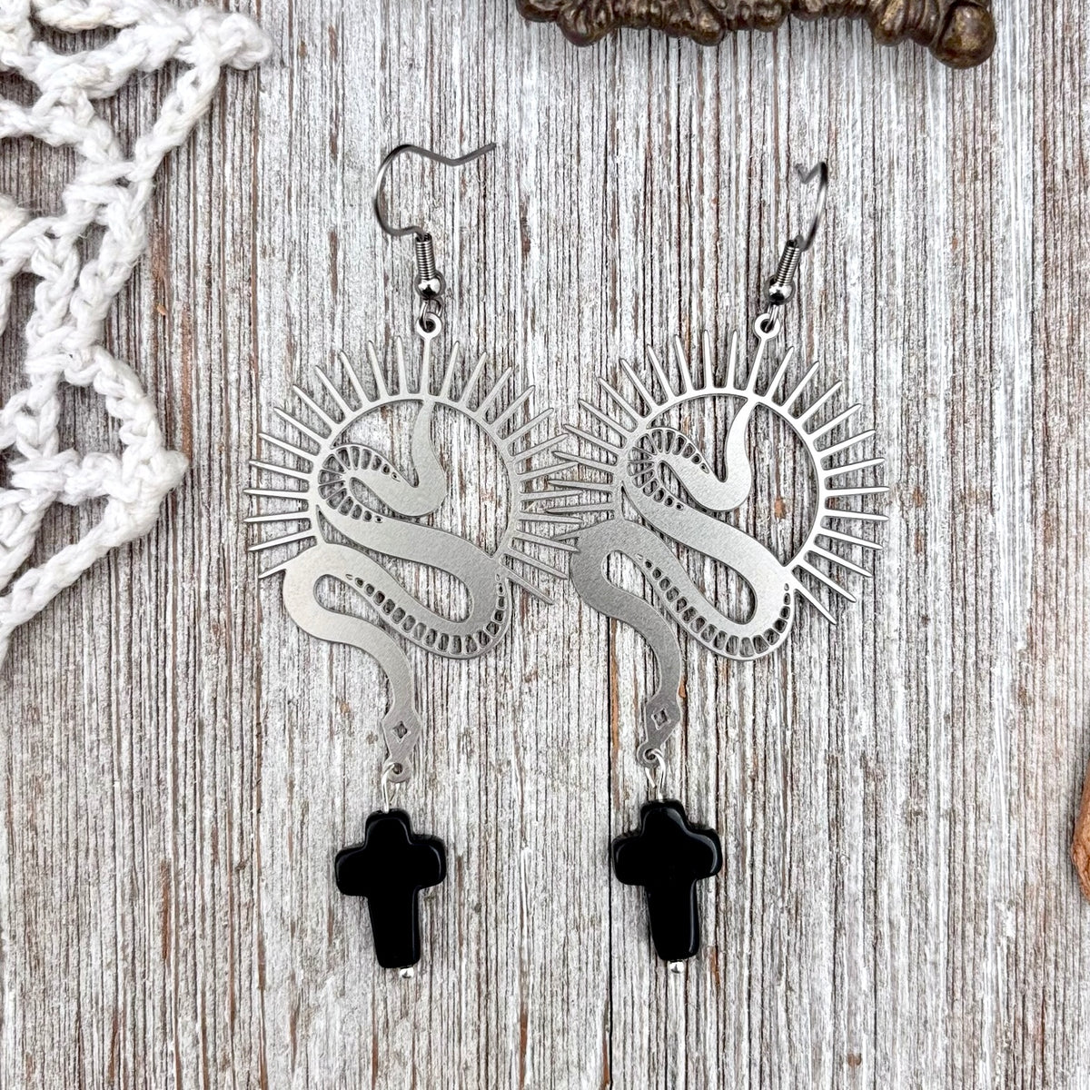 Stainless steel snake and black cross dangle earrings by FOXLARK, featuring long, intricate earring designs with metal and dark accents.